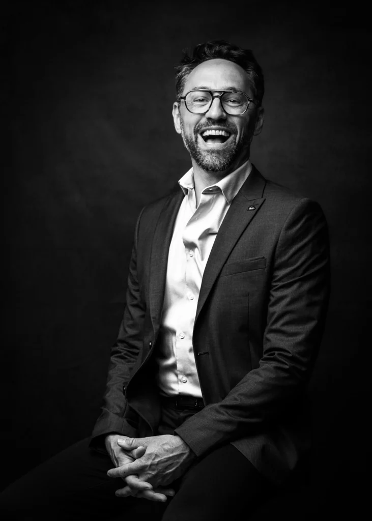 Portrait professionnel d’un homme en costume, sourire naturel, en noir et blanc.