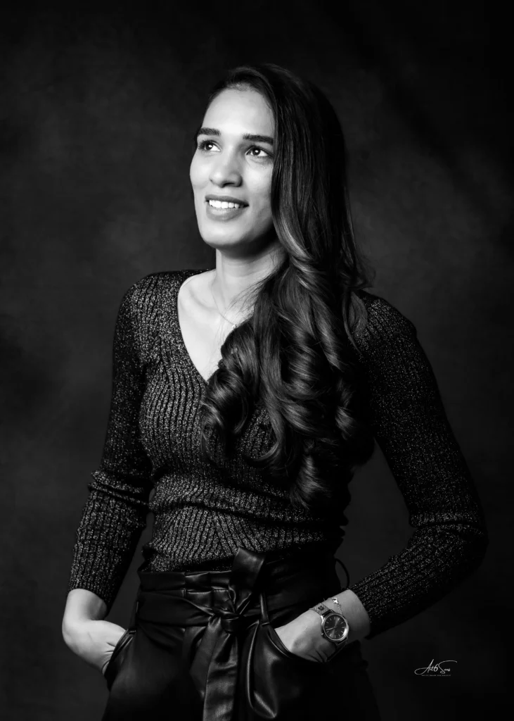 Portrait professionnel en noir et blanc d’une femme souriante, debout, mains dans les poches.