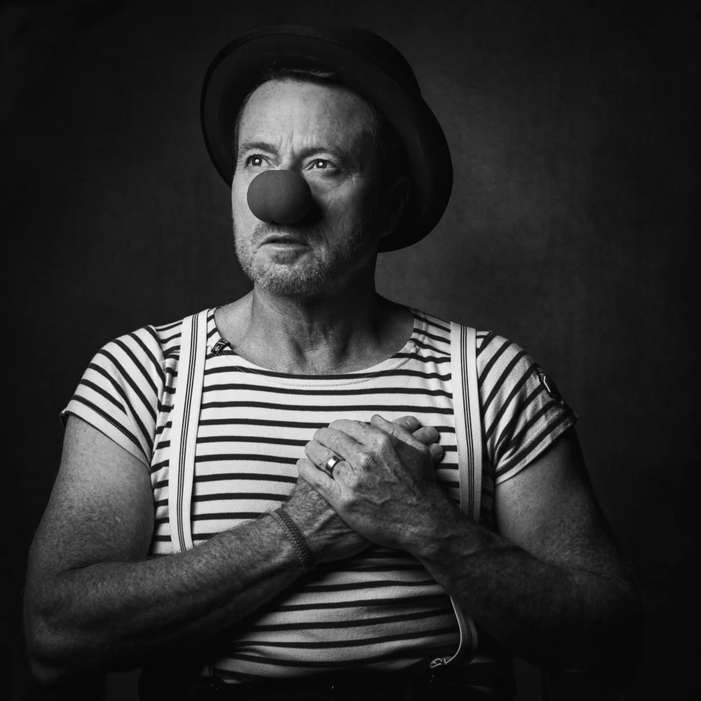 Portrait en noir et blanc d’un homme habillé en clown avec un nez rouge et un chapeau, réalisé par Art6Sens, Portraitiste de France à La Teste.