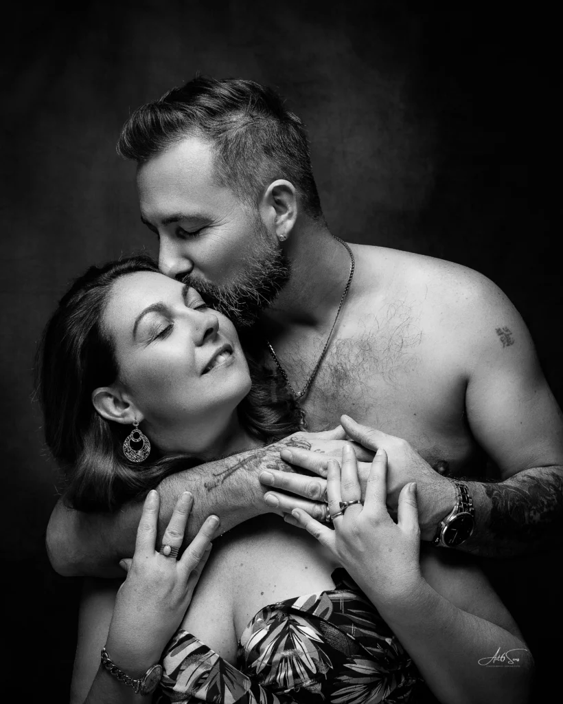 Portrait en noir et blanc d’un couple enlacé, l’homme torse nu embrassant tendrement la femme. Photographie intime et expressive signée Art6sens