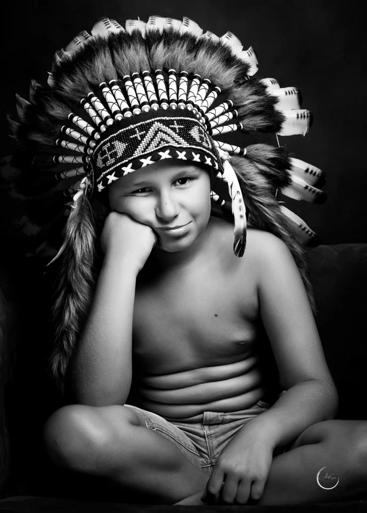 ortrait noir et blanc d'un enfant coiffé d'une grande parure à plumes, regard espiègle, studio Art6sens Bassin d'Arcachon