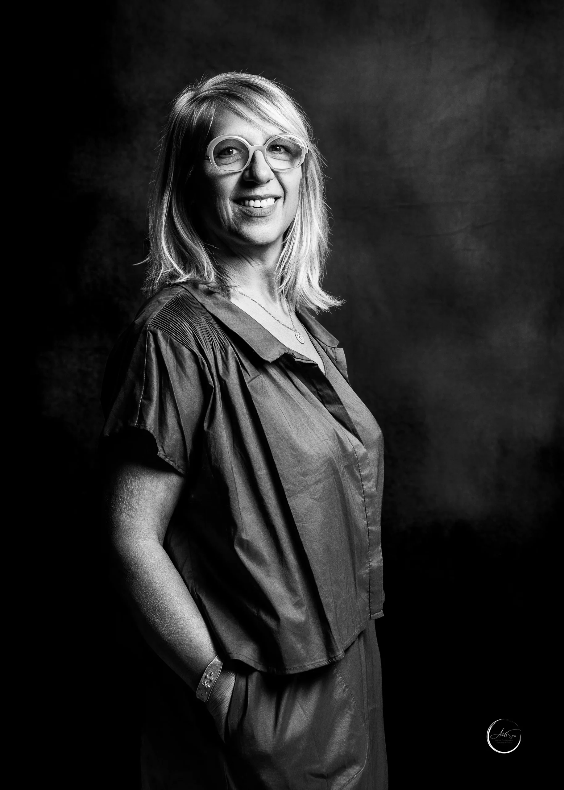 Portrait professionnel noir et blanc d'une femme entrepreneur souriante, lunettes rondes, studio Art6sens Bassin d'Arcachon
