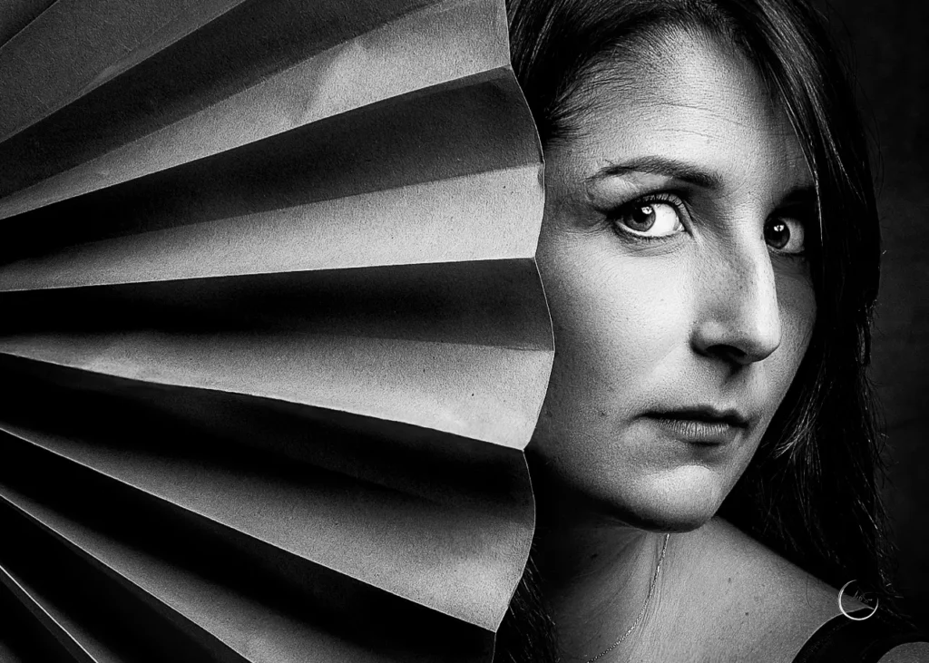 Portrait noir et blanc en gros plan, visage de femme à demi caché par un éventail, regard intense, Art6sens Bassin d'Arcachon