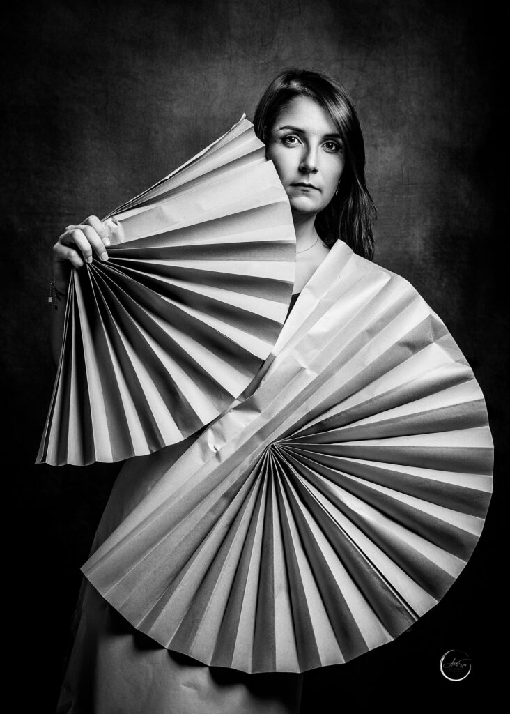 Portrait noir et blanc d'une femme tenant un grand éventail devant son visage, regard intense, studio Art6sens Bassin d'Arcachon