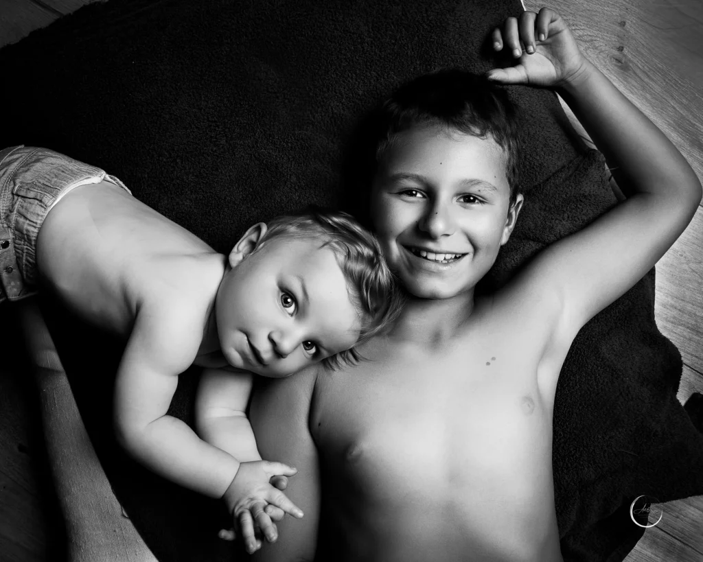 Portrait noir et blanc de deux frères allongés, bébé et grand frère complices, studio Art6sens Bassin d'Arcachon
