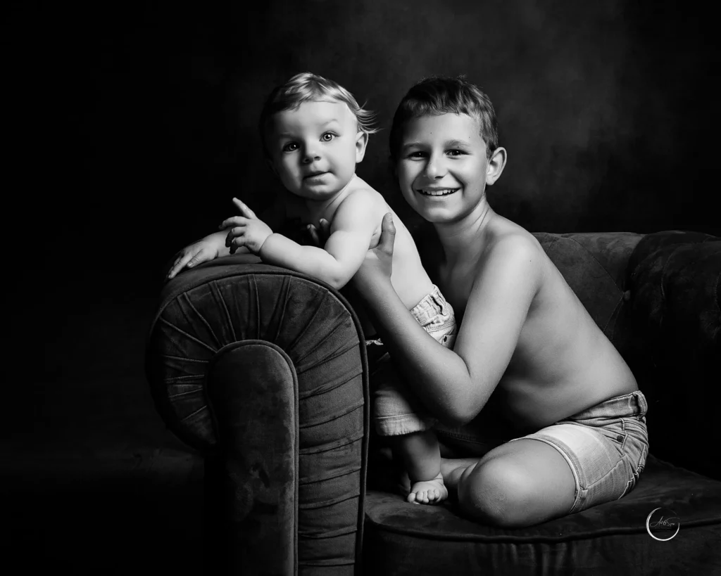 Portrait noir et blanc de deux frères sur un fauteuil en velours, bébé et grand frère, studio Art6sens Bassin d'Arcachon