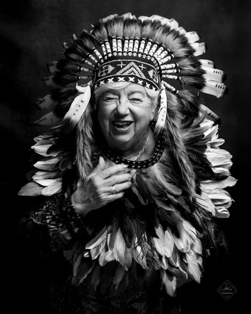 Portrait noir et blanc d'une femme senior riant aux éclats avec une coiffe à plumes, studio Art6sens Bassin d'Arcachon